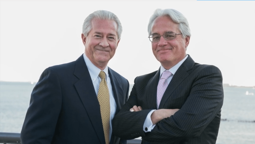 Bob Enk and a professional colleague smiling in business attire against an outdoor waterfront backdrop for MiniMatters video production.