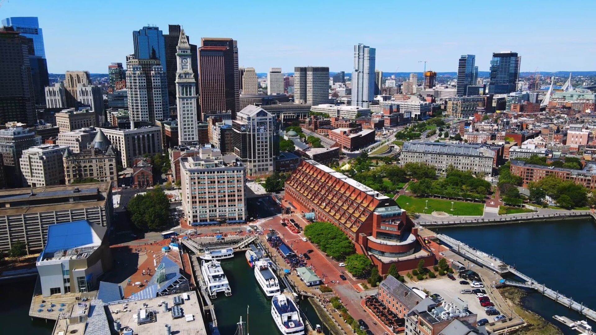 Aerial view of a waterfront city skyline with high-rise buildings, marinas, and a busy harbor area on a clear day.