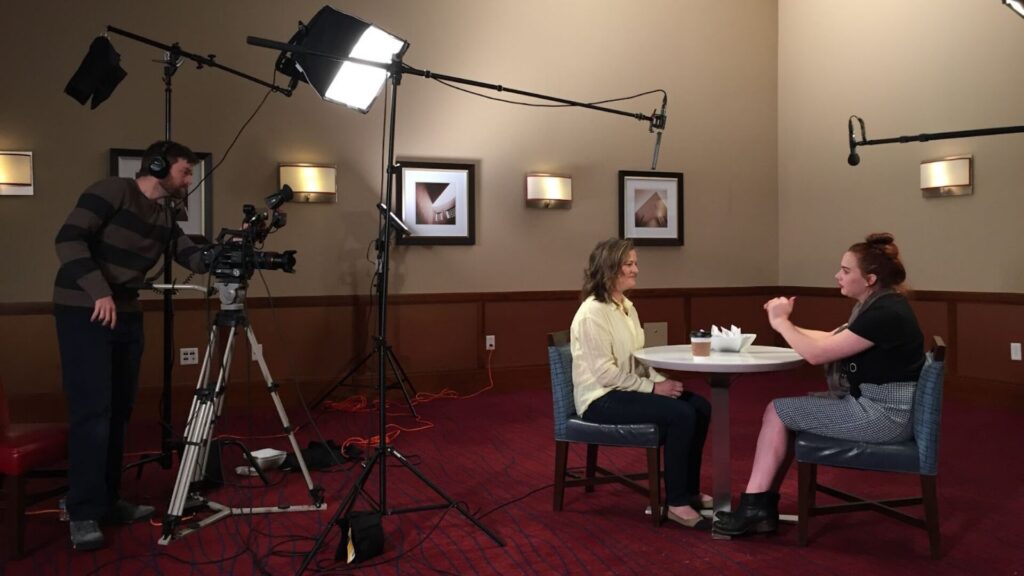 2 women sitting at a table and a man using a camera to record them talking | video production services Washington DC