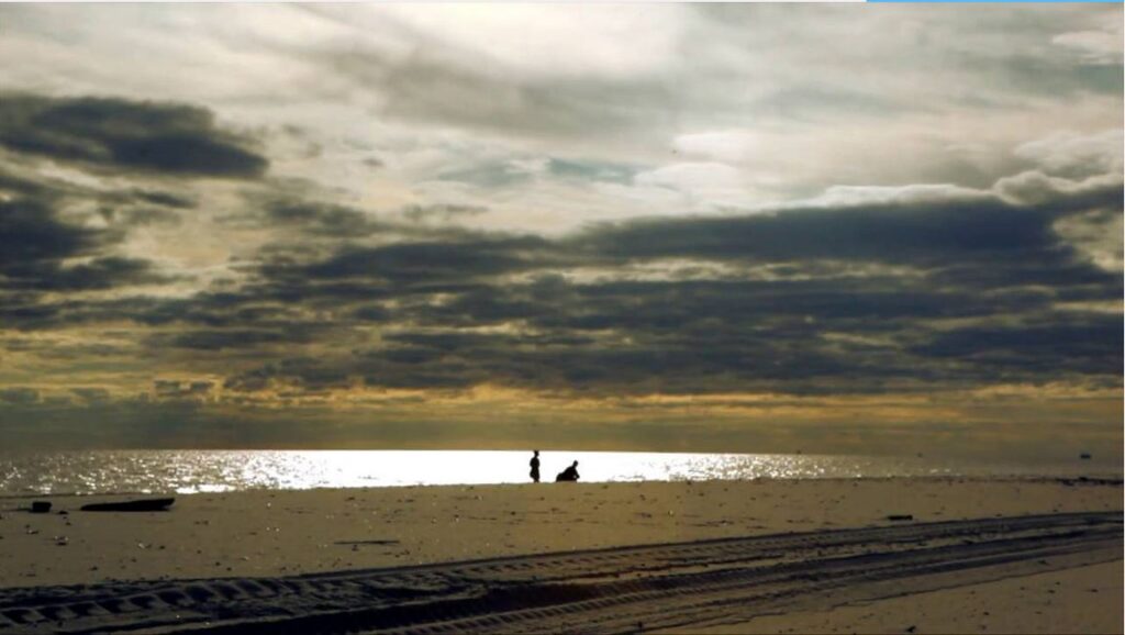 Silhouettes of two people on ocean beach at sunset in storytelling video scene