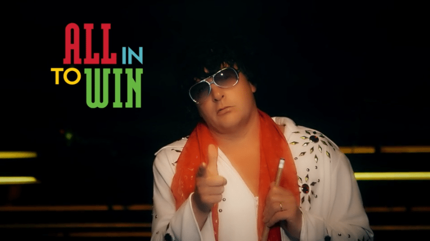 Person dressed in an Elvis-style costume pointing toward the camera with text “All In to Win” on the left.