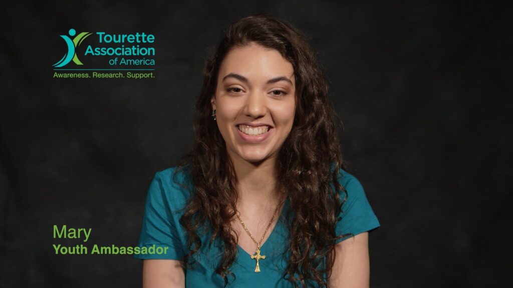 A smiling Tourette Association of America Youth Ambassador named Mary in a professional video interview setting.