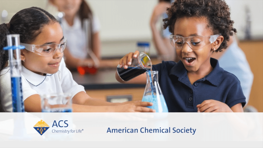 Two young students wearing safety goggles smile while conducting a chemistry experiment for an American Chemical Society (ACS) educational video.