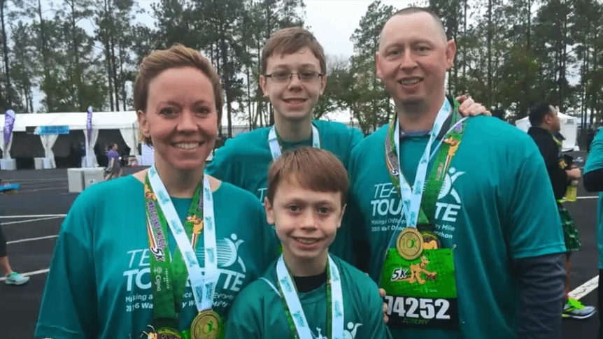 A family of four wearing Team Tourette t-shirts and finisher medals at a 5K fundraising event.