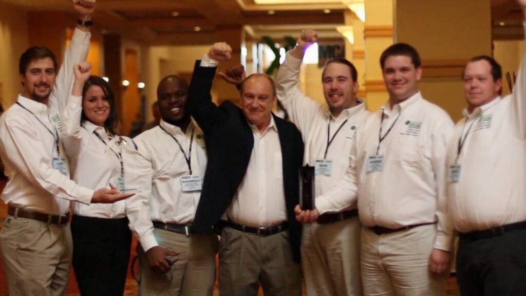 A team of diverse professionals in matching white shirts raising their fists in celebration during an award presentation.